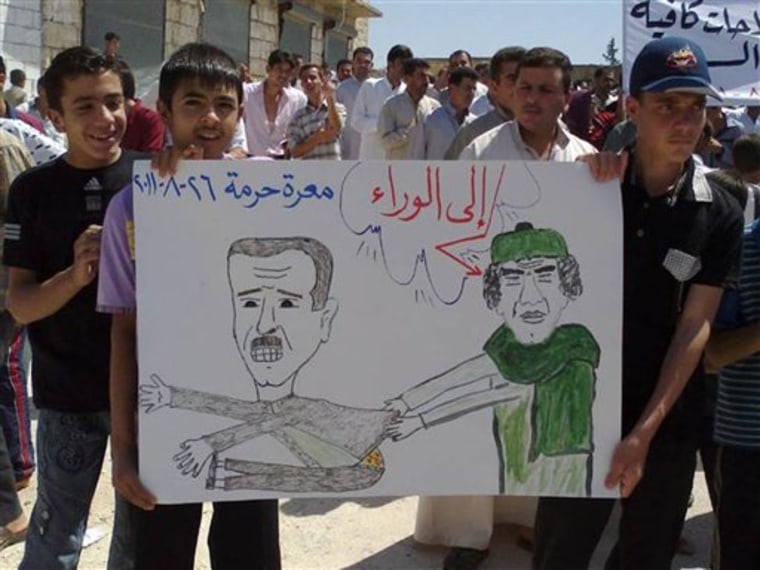 In this citizen journalism image made on a mobile phone and provided by Shaam News Network, protesters against Syrian President Bashar Assad hold a cartoon placard depicting Moammar Gadhafi, right, and Assad, left, with Arabic words reading: "Step back," during a demonstration against the Syrian regime, at Maaret Harma village, in Edlib province, Syria, on Friday.